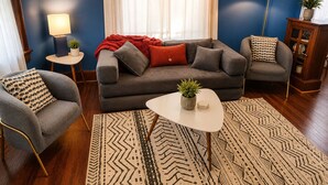 A living room with a sofa, two armchairs, a coffee table, a rug, a lamp, and a side table with a plant.