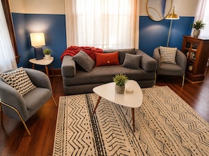 A living room with a sofa, two armchairs, a coffee table, a rug, a lamp, and a side table with a plant.