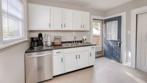 A modern kitchen with white cabinets, a stainless steel dishwasher, a coffee maker, and a sink.