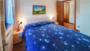 A bedroom with a bed, a nightstand, a lamp, a painting, and a door. - Nice apartment for 4 guests with TV and pets allowed (Canazei)