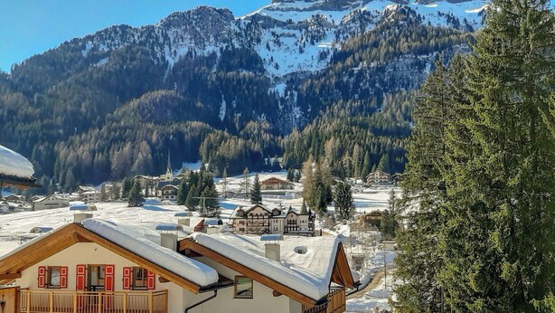 A snow-covered mountain village with traditional wooden houses and a church. - Nice apartment for 4 guests with TV and pets allowed (Canazei)