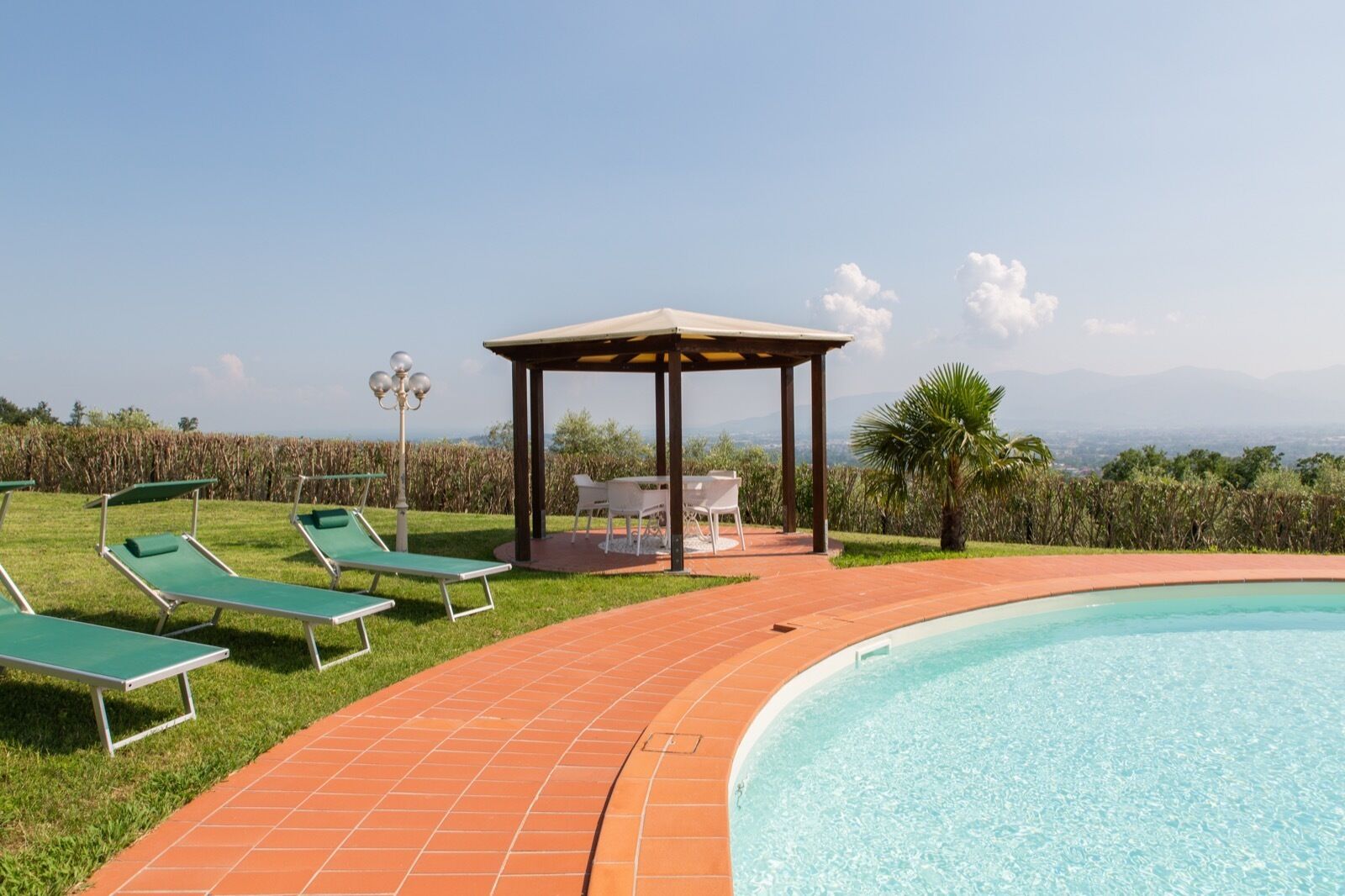 A pool area with green lounge chairs, a covered seating area, and a view of distant mountains.