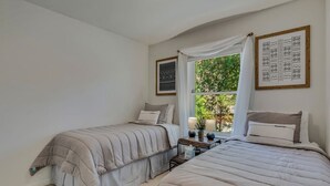 A bedroom with two beds, a nightstand, a window with curtains, and framed artwork on the walls. - Peaceful & Spacious Home with Sauna • Sleeps 12 (Glenwood Springs)