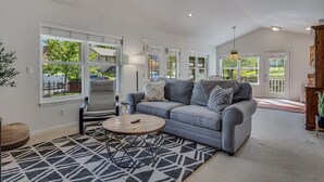A spacious living room with a grey sofa, a patterned rug, and large windows offering a view of the outdoors. - Peaceful & Spacious Home with Sauna • Sleeps 12 (Glenwood Springs)
