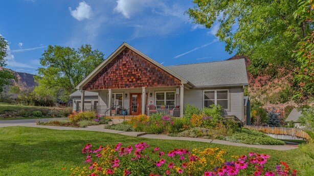 A two-story house with a prominent wooden gable roof, a front porch with a railing, and a well-maintained garden with colorful flowers. - Peaceful & Spacious Home with Sauna • Sleeps 12 (Glenwood Springs)
