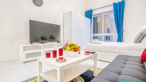 A modern living room with a flat-screen TV, white furniture, a fruit bowl, red candles, and a sofa. - MK Residence By Be Our Guest (Dubai)