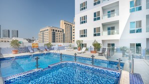A rooftop swimming pool with lounge chairs and potted plants, surrounded by modern buildings. - MK Residence By Be Our Guest (Dubai)