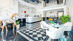 A modern hotel lobby with a marble reception desk, a check-in counter, a seating area with white chairs, and a decorative horse sculpture. - MK Residence By Be Our Guest (Dubai)