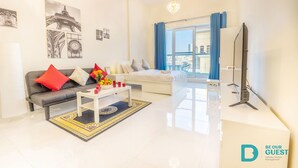 A modern living room with a grey sofa, white coffee table, and a large window with blue curtains. - MK Residence By Be Our Guest (Dubai)