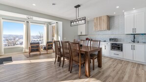 A modern kitchen with white cabinets, a wooden dining table, and a view of the city through large windows. - 1 bedroom and kitchen place with a valley scenery view & free parking (CALGARY)