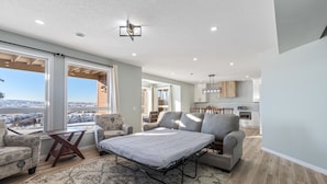 A spacious living room with a large window, a sofa, a coffee table, and a view of the city. - 1 bedroom and kitchen place with a valley scenery view & free parking (CALGARY)