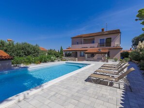 Relax by the pool surrounded by lush greenery and a clear sky.