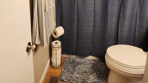 Et badeværelse med bruseforhæng, toilet, håndklæderække med håndklæde og toiletpapirholder.