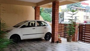 Katettu pysäköintialue, jossa on valkoinen auto parkissa. Alueella on myös ruukuissa olevia kasveja ja laatoitettu lattia.