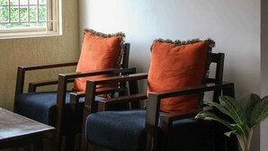 Huoneessa on kaksi puista tuolia, joissa on oranssit tyynyt, pieni pöytä ja ruukussa oleva kasvi.