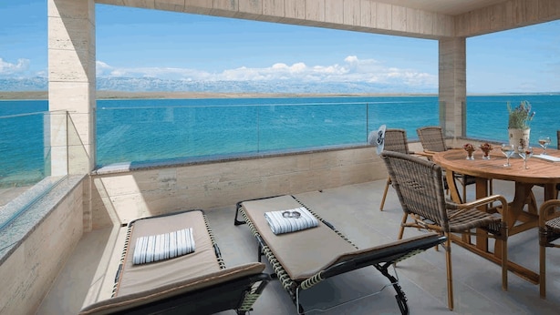 Un balcon doté de chaises longues et d’une table à manger, offrant une vue sur une vaste étendue d’eau.
