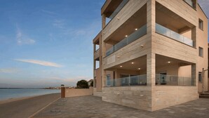 Un immeuble moderne à plusieurs étages, doté de balcons, d’une allée pavée et offrant une vue sur la mer.