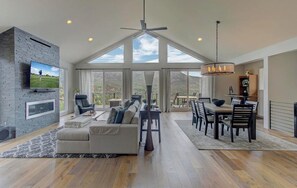 A spacious living room with a large TV, a fireplace, and a dining area with a chandelier.