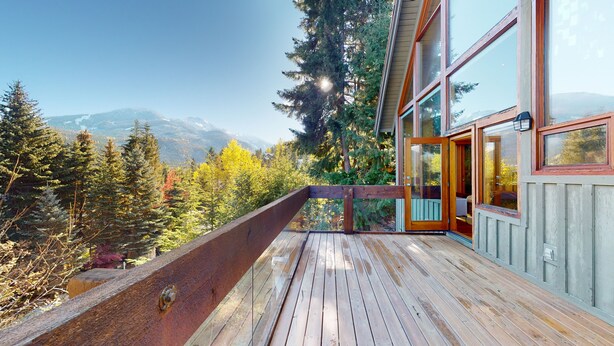 A wooden deck with a glass balustrade overlooking a forested mountain landscape. - Stunning 3 Bedroom / 3.5 Bathroom Blueberry house with breathtaking Mountain Views (Whistler)