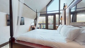 A bedroom with a large bed, a TV, a window with a view of trees, and a balcony. - Stunning 3 Bedroom / 3.5 Bathroom Blueberry house with breathtaking Mountain Views (Whistler)