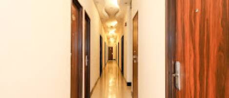 Un pasillo de hotel con puertas de madera a ambos lados, suelo de baldosas e iluminación empotrada en el techo.
