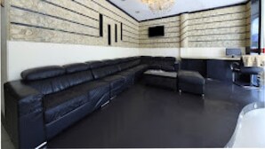 A modern living room with a black sectional sofa, a flat-screen TV mounted on the wall, and a decorative ceiling light fixture. - GOLDEN PALACE HOTEL (Kuala Lumpur)