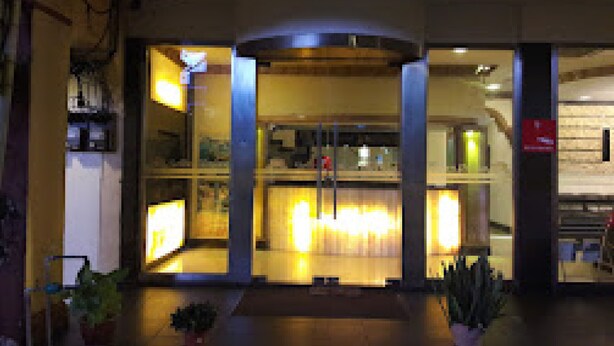 A hotel entrance with a glass facade, a central illuminated pillar, and potted plants at the entrance. - GOLDEN PALACE HOTEL (Kuala Lumpur)