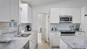 Una cocina moderna con armarios blancos, un lavamanos de acero inoxidable, una cafetera y un microondas.
