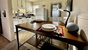 Une cuisine compacte avec des meubles blancs, un four à micro-ondes, un réfrigérateur et une table à manger, ainsi que des assiettes et un verre à vin.