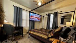 Une chambre d’hôtel équipée d’un lit, d’un bureau, d’une chaise, d’une télévision et d’un ventilateur de plafond.