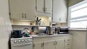 Une cuisine de taille réduite avec des meubles blancs, une cuisinière, un four à micro-ondes et un évier.