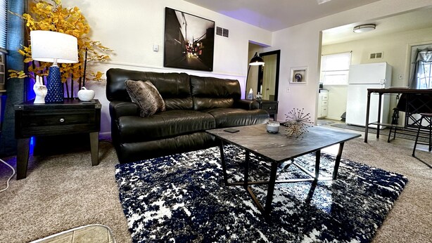 Un salon avec un canapé en cuir noir, une table basse, une lampe sur pied et un ventilateur de plafond.