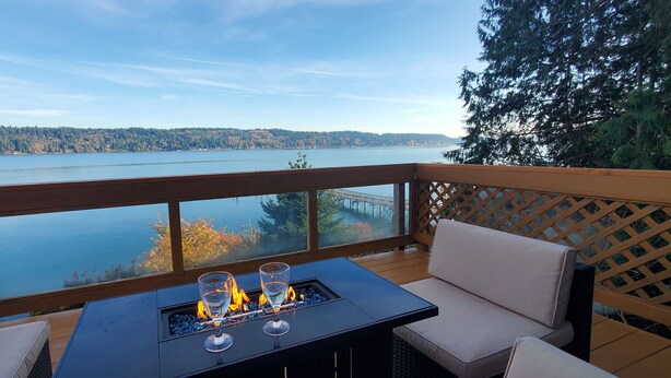 A deck with a fire feature, seating, and a view of a lake and forest. - Waterfront Home w/ Mt Rainier Views, Private Beach, 4 Decks, Sleeps 9 (Bremerton)