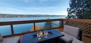 A deck with a fire feature, seating, and a view of a lake and forest. - Waterfront Home w/ Mt Rainier Views, Private Beach, 4 Decks, Sleeps 9 (Bremerton)