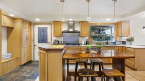A modern kitchen with wooden cabinets, a central island with stools, and pendant lighting. - Waterfront Home w/ Mt Rainier Views, Private Beach, 4 Decks, Sleeps 9 (Bremerton)