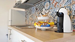 Una cuina amb una cafetera, un cistell d'aperitius i una rebentada de rajola.