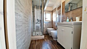 Un bany modern amb un espai de dutxa de vidre, un vàter i un lavabo amb mirall a la part superior.