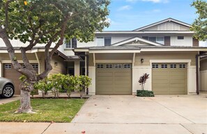 A two-story house with a garage, a driveway, and a tree in the front yard.