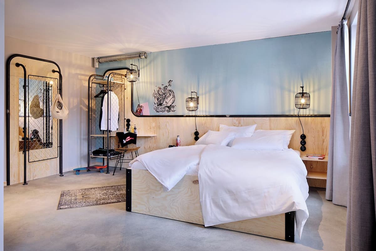 Un dormitorio moderno con una cama grande, cabecera de madera, espejo y una lámpara fijada a la pared.