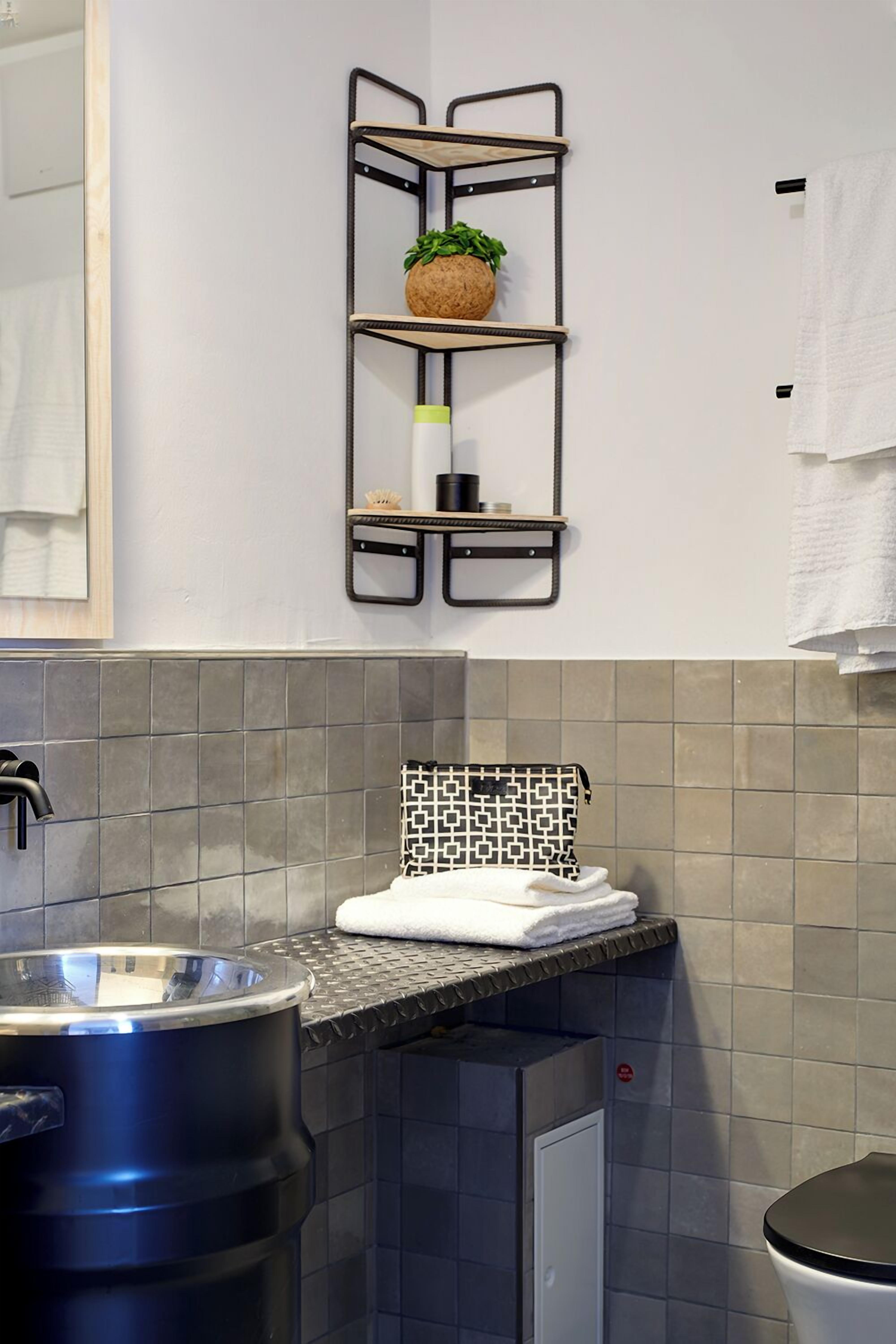 Une salle de bain avec une étagère en métal où sont rangés les articles de toilette, un porte-serviettes et un pare-éclaboussures carrelé.
