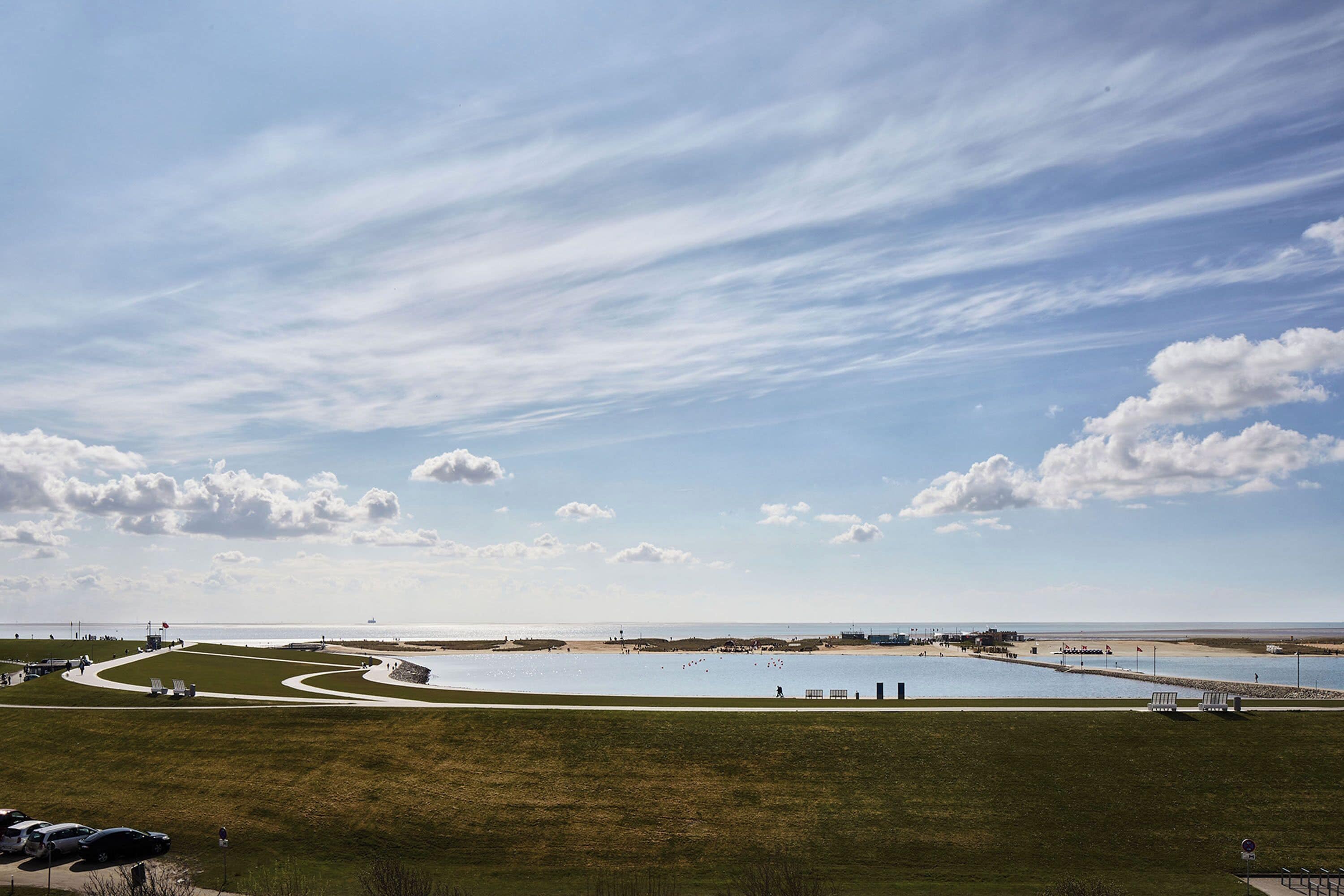 A coastal landscape with a grassy area, a sandy beach, and a body of water.