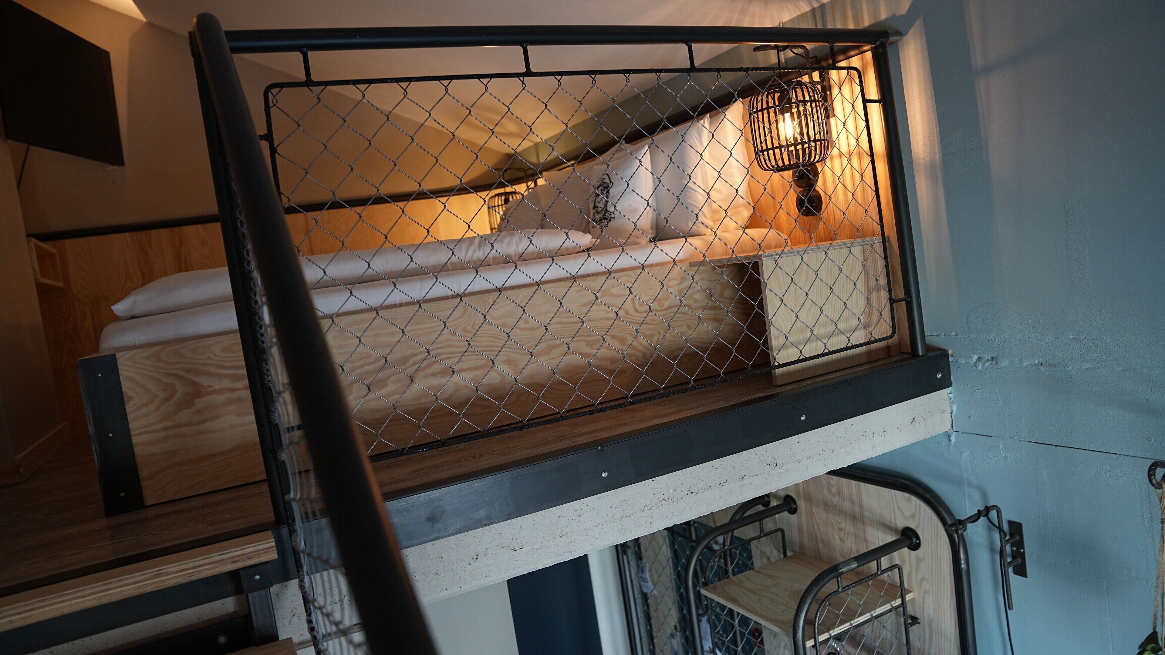 Ein Stockbett mit Metall-Schutzgitter und einem kleinen, abgeschlossenen Bereich mit einer Lampe.