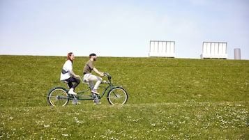 Dos personas andando en bicicleta sobre un campo césped con estructuras blancas al fondo.