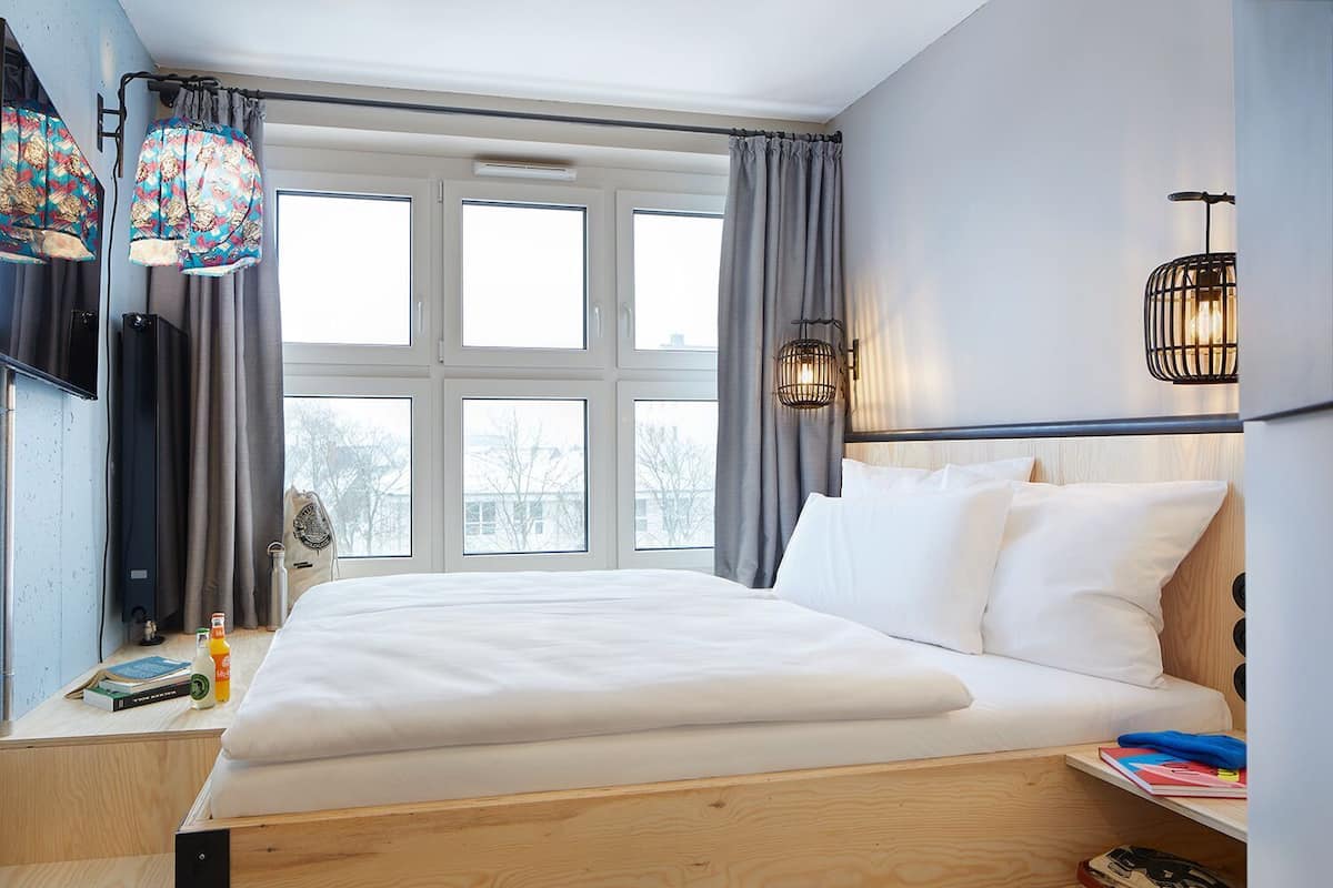 Una habitación de hotel con una cama grande, varias ventanas, un televisor y dos lámparas fijadas a la pared.
