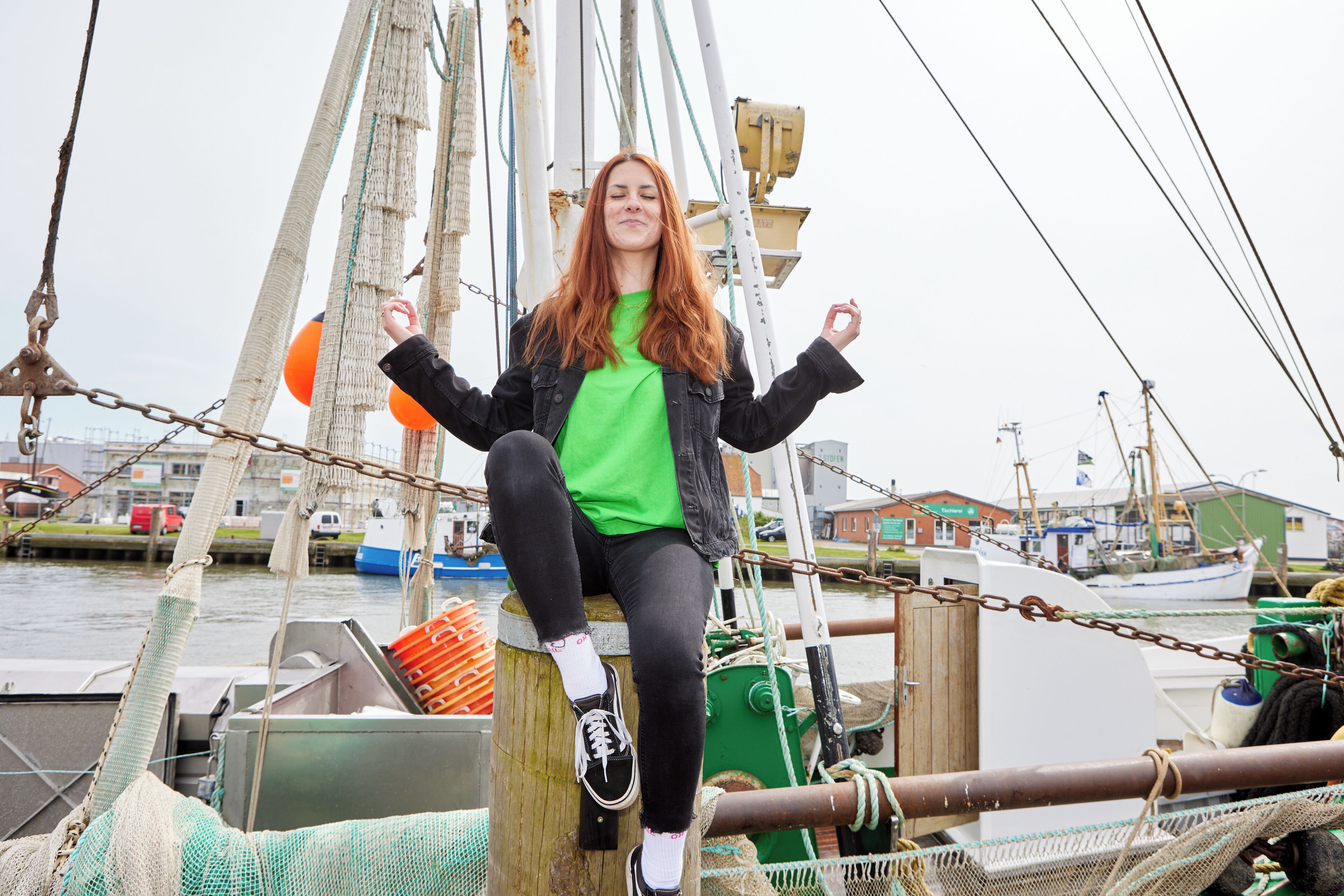 A person sitting on a dock with a boat in the background.