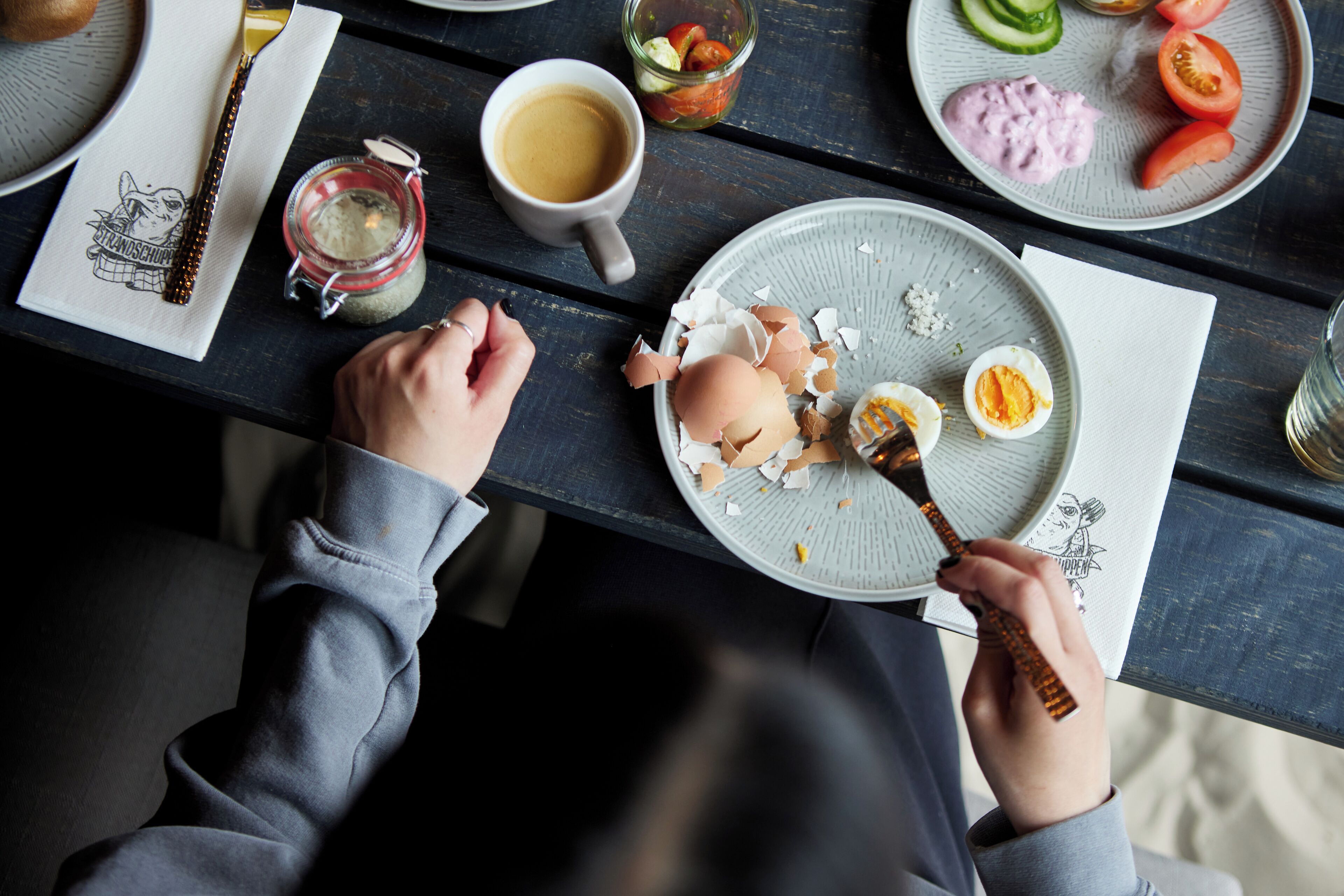 Une table à manger avec une assiette de nourriture, une tasse de café et un pot de confiture.
