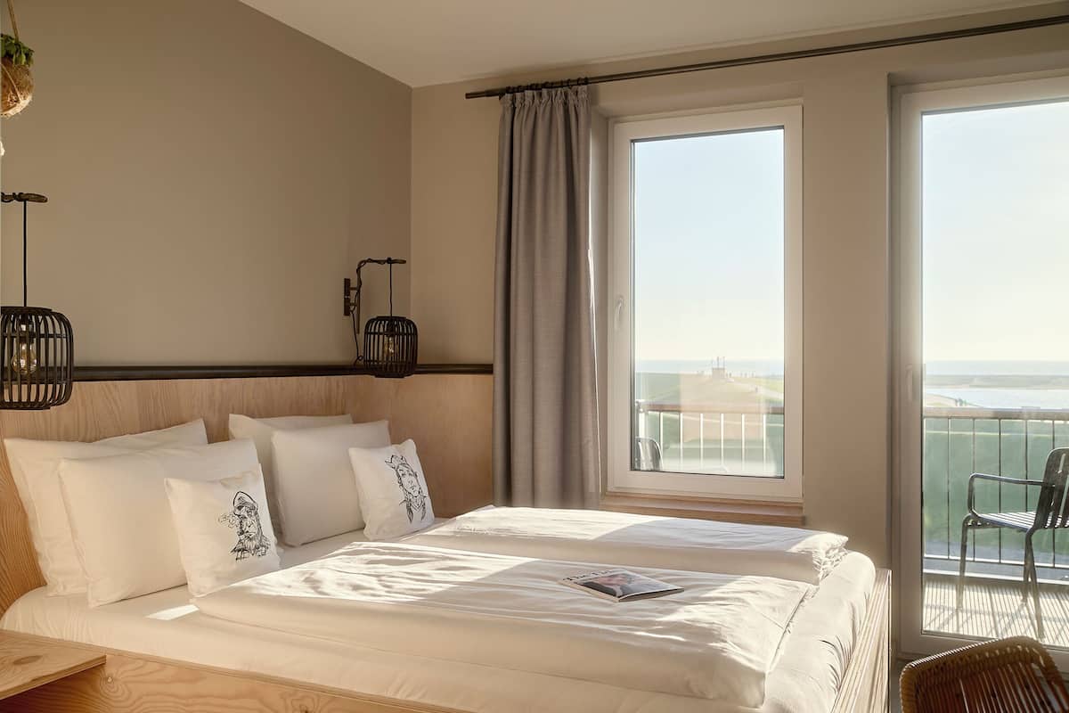 Habitación de hotel con una cama grande, vistas al mar y un balcón con una silla.