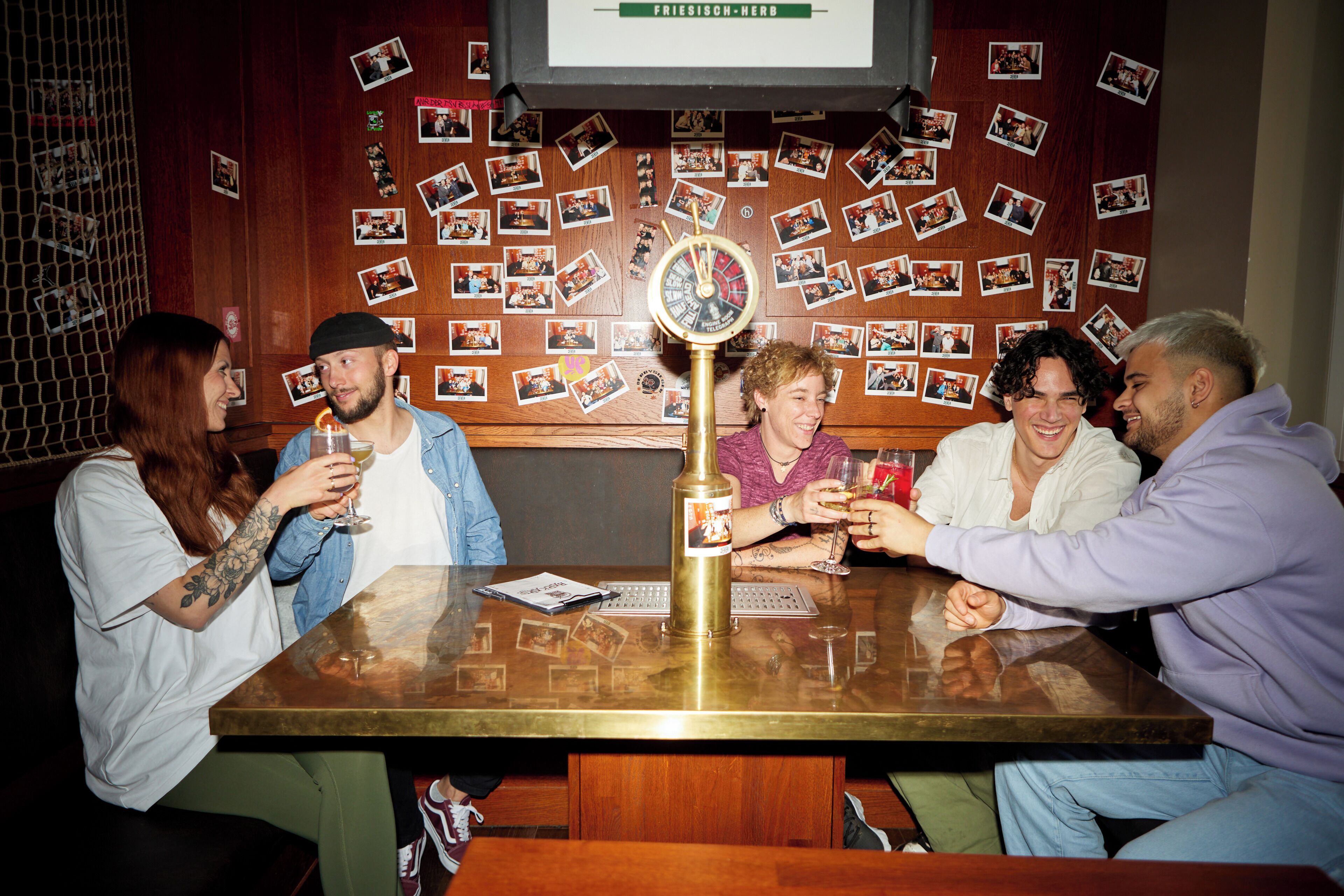 A group of people sitting around a table with a clock in the center, surrounded by a wall decorated with photos.