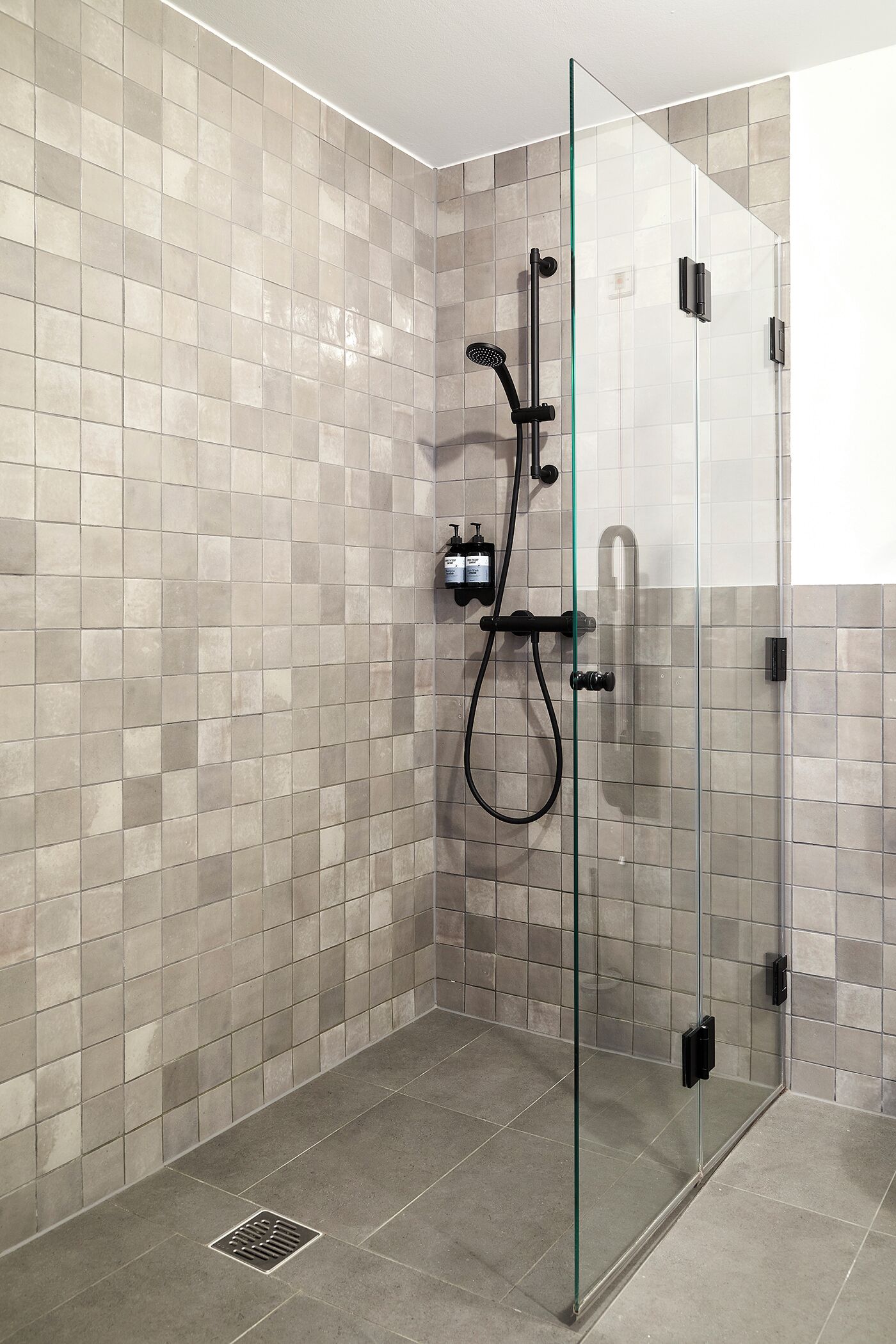 A glass-enclosed shower with a tiled wall, a handheld showerhead, and a control panel.