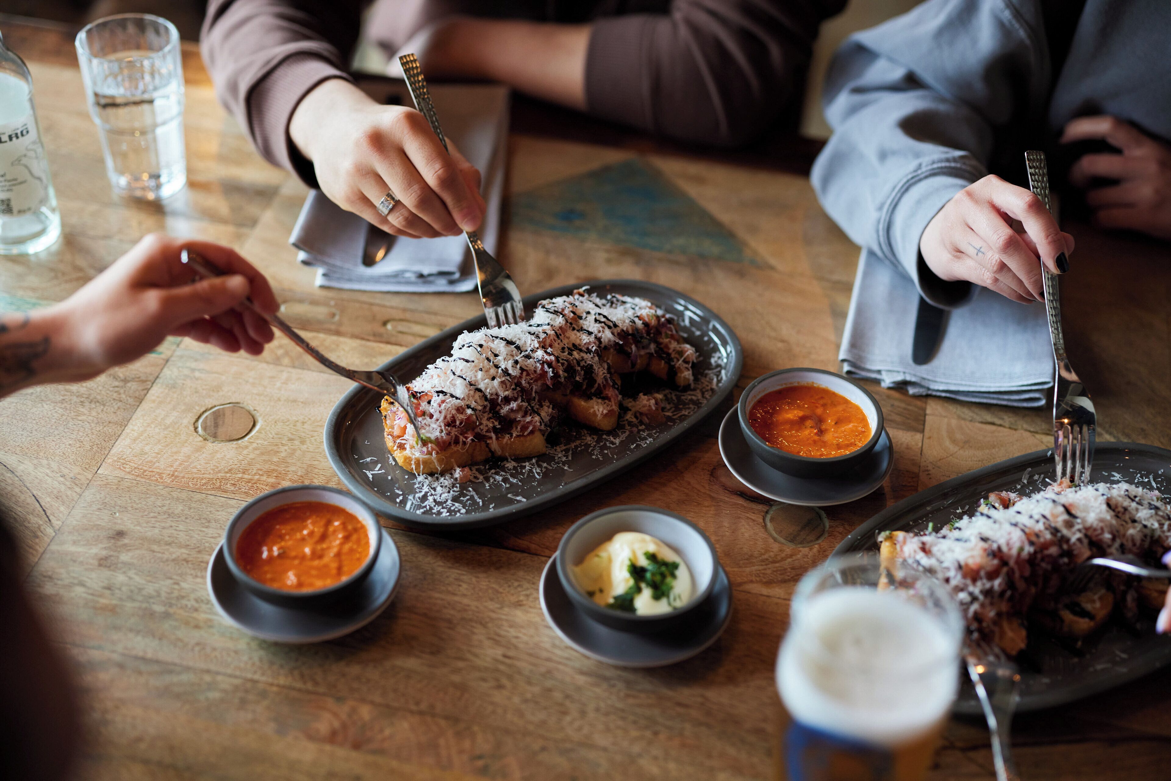 A wooden table with plates of food, bowls of sauces, and glasses of water.